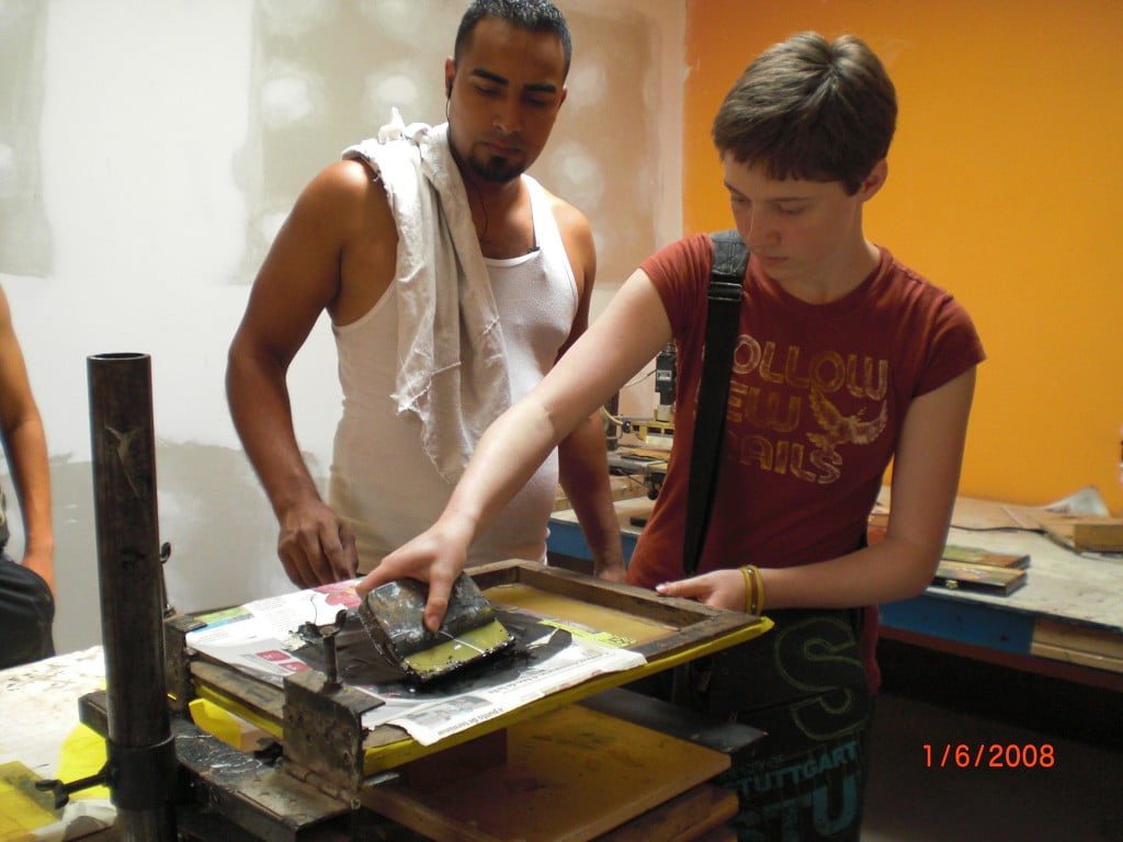 Miranda and employee teaching her how to screen print a design on a tobacco box lid