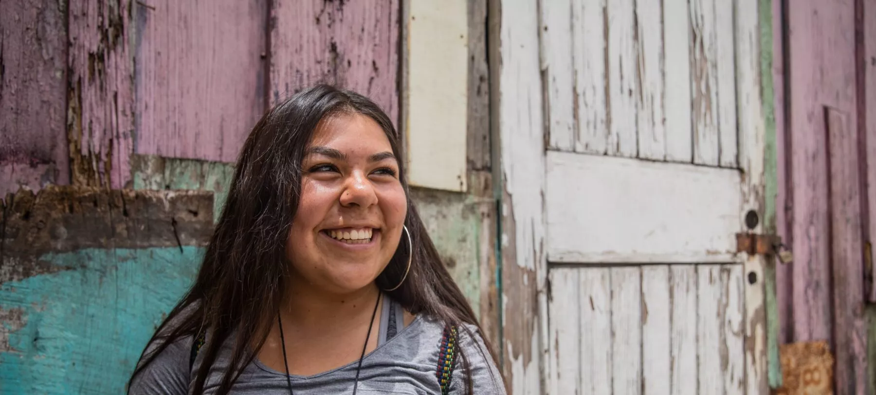 Girl smiling at something off camera in front of a pastel painted wooden structure